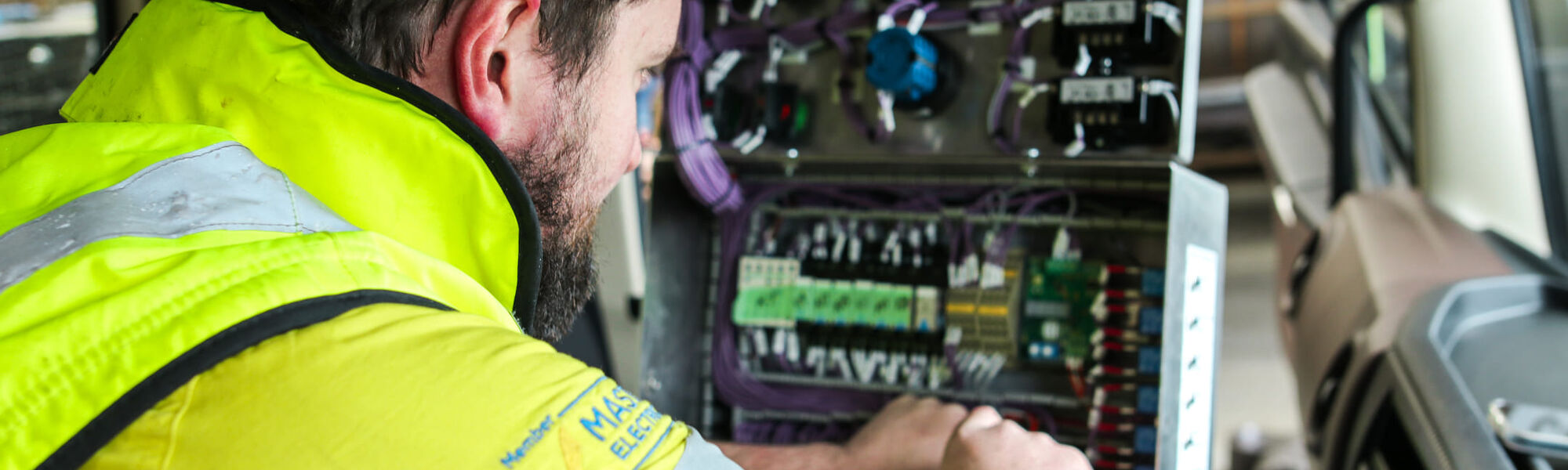 Technician wiring an electrical control panel inside a truck cab