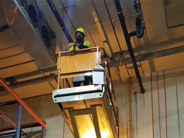 Technician on a scissor lift inspecting overhead refrigeration ductwork